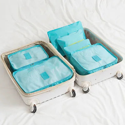 A white clothes storage organizer set with six teal fabric storage boxes is shown on a white bed.