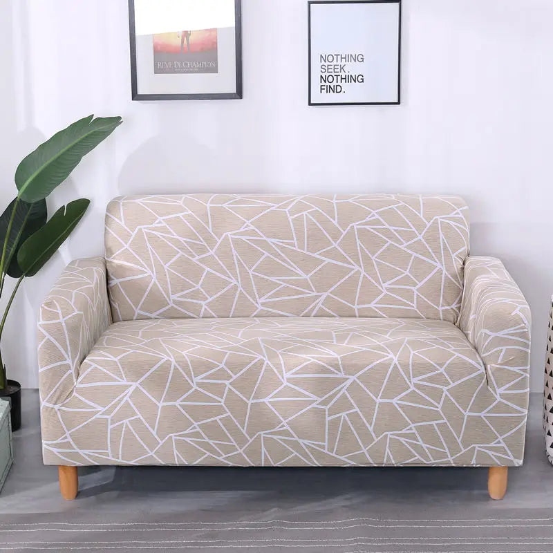 A beige stretch floral elastic sofa cover displayed on a light gray floor with framed art on the white wall.