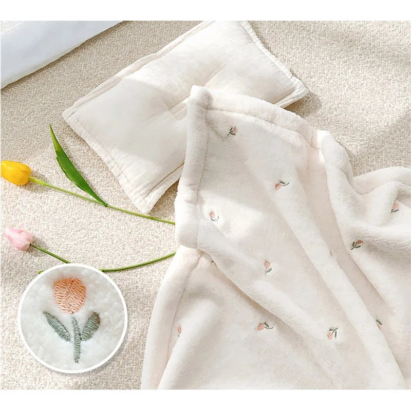 A soft, cream-colored coral fleece flannel blanket is displayed next to a yellow flower and a pink flower.