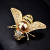 A gold and diamond crystal bee brooch featuring a pearl accent on the body and wings.