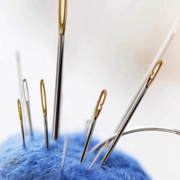 A close-up of a precision self-threading sewing needle kit with various gold and silver needles placed on a blue felt backgro