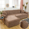 A beige L-shaped sofa protector cover placed on a light wood floor in a bright living room.