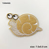 A tan embroidered patch of a sea turtle with large eyes and a spiral pattern.