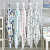 Five white muslin swaddle blankets with colorful floral and geometric patterns hanging on a metal rack
