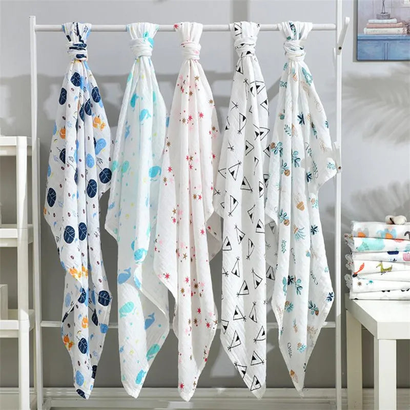Five white muslin swaddle blankets with colorful floral and geometric patterns hanging on a metal rack