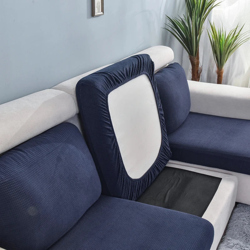 A dark blue stretch sofa seat cushion protector slipcover placed on a white sofa seat.