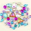 A collection of colorful silver claw rhinestones and gemstone-like decorations scattered on a white background.