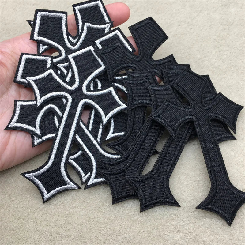 Several black and white embroidered cross applique patches are held in a hand against a light background.