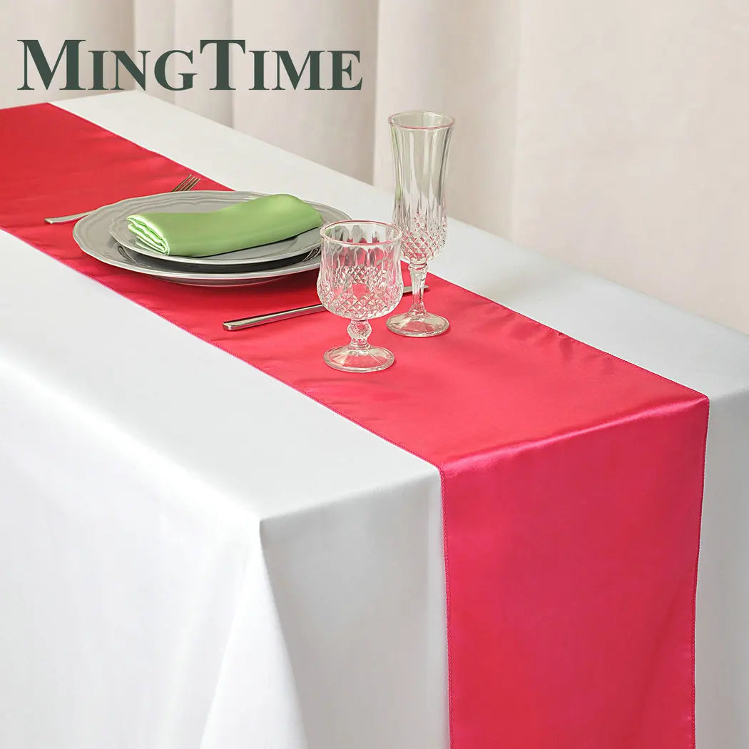 Elegant satin pink table runner with silverware and glassware set on a white tablecloth