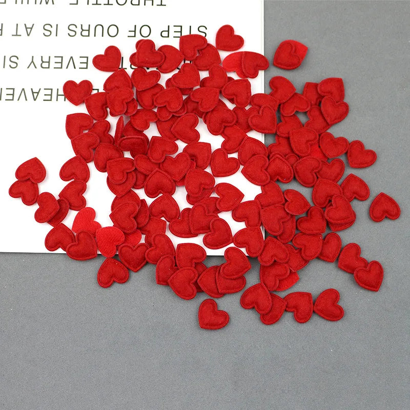 A pile of bright red felt heart appliques scattered on a gray surface.