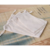A set of ten natural cotton drawstring gift bags laid out on a bamboo mat.