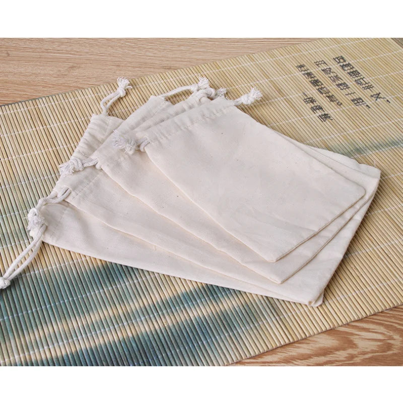A set of ten natural cotton drawstring gift bags laid out on a bamboo mat.