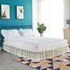 A white bed with a lace ruffle skirt and elastic trim sits in a room featuring teal walls and natural light.