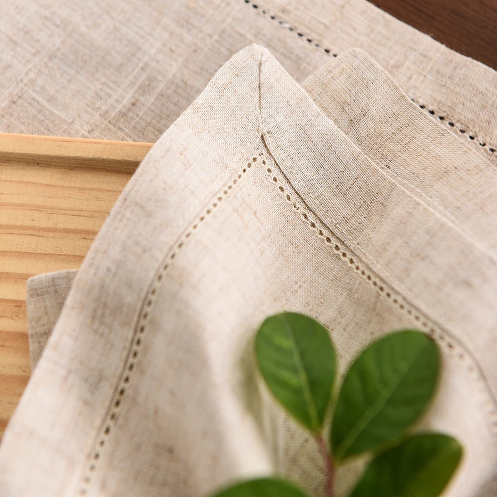 Close-up of a beige linen napkin with visible stitching and a green plant leaf.