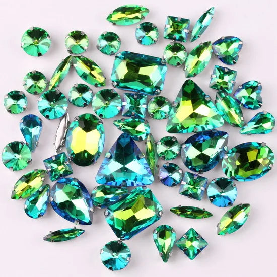 A scattering of green and blue faceted gemstone rhinestones on a white background.