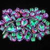 A close-up of a set of vibrant green and purple gemstone rhinestones arranged in a decorative pattern.