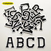 A collection of black and white alphabet letter embroidery patches scattered on a white background.