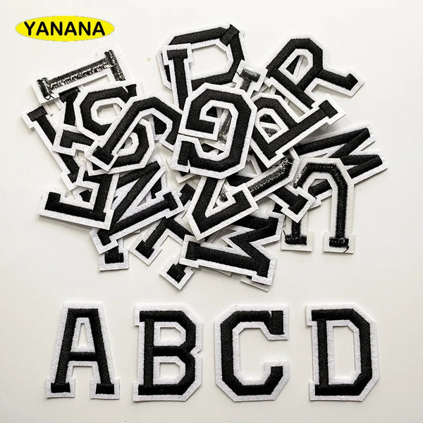 A collection of black and white alphabet letter embroidery patches scattered on a white background.