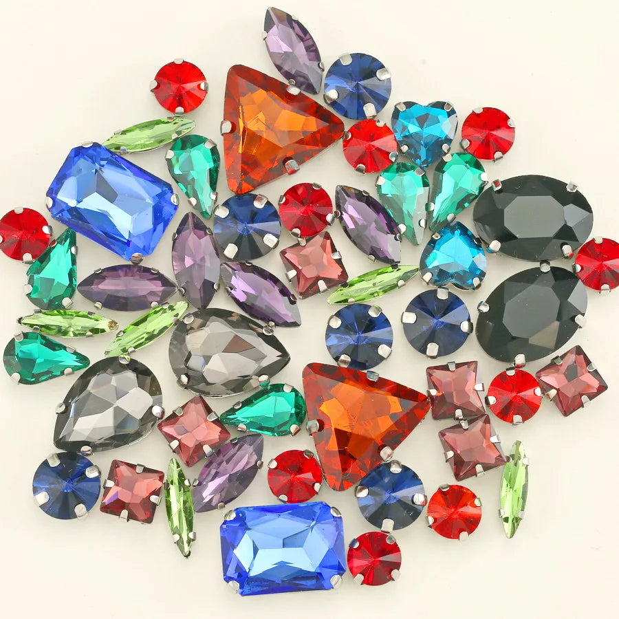 A collection of 50 various colored and cut silver claw rhinestones scattered on a white background.