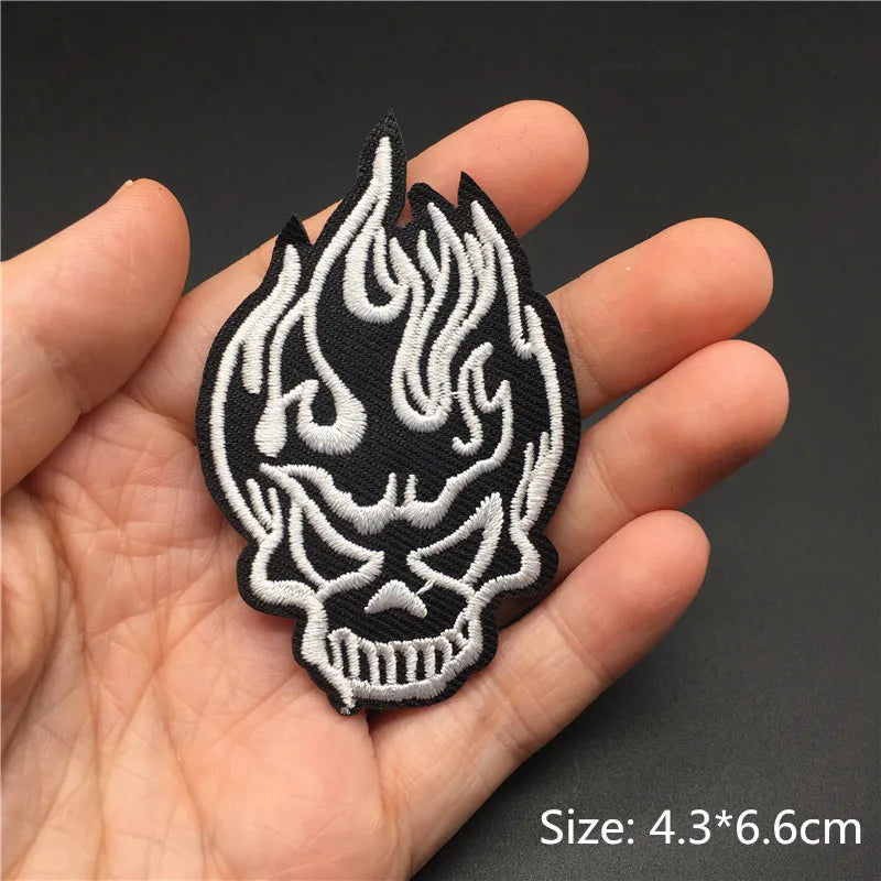 A hand holds an embroidered punk skull design badge on a black fabric background.