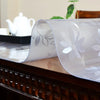 A sheer, translucent gray PVC tablecloth draped over a wooden surface with white floral patterns.