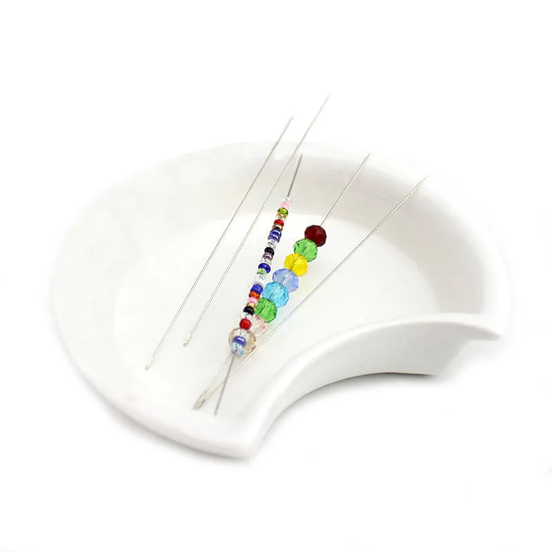 A set of precision stainless steel beading needles with colorful beads displayed on a white dish.