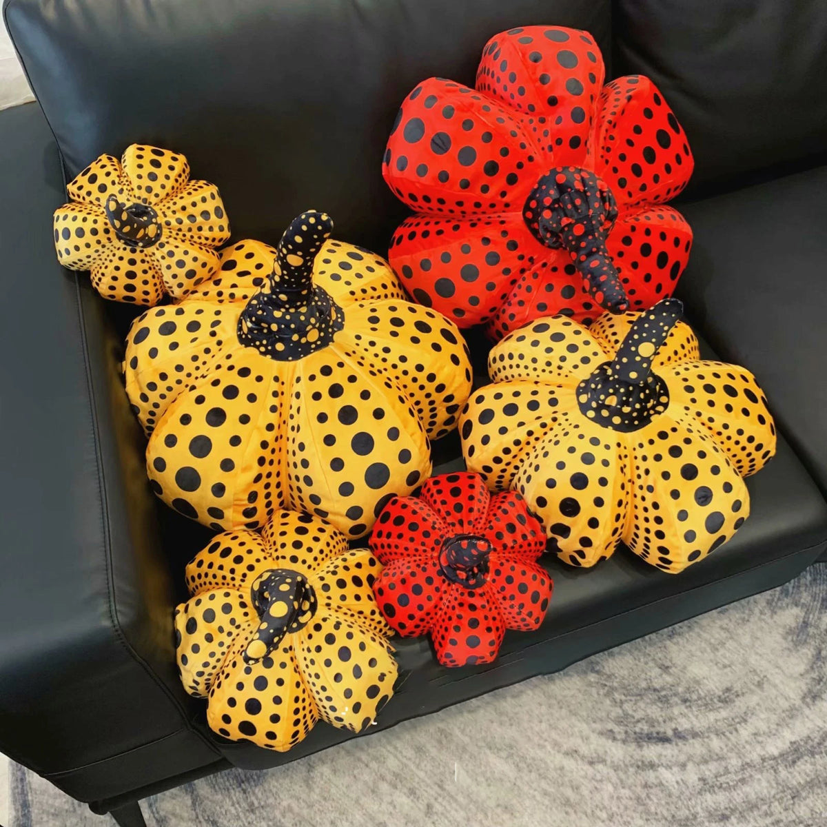 A collection of orange and red polka-dotted pumpkin plush cushions displayed on a black leather sofa.