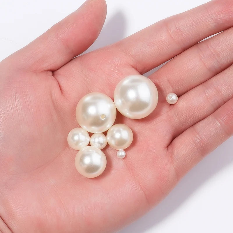A hand holds several round, white imitation pearl beads for DIY jewelry making.