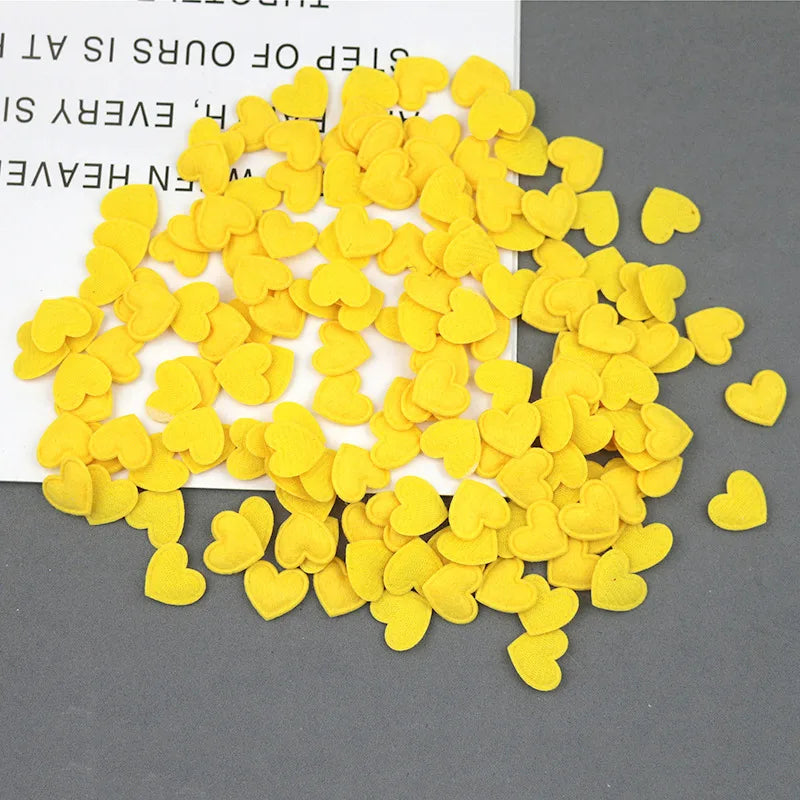 A pile of yellow felt heart appliques scattered on a gray surface.