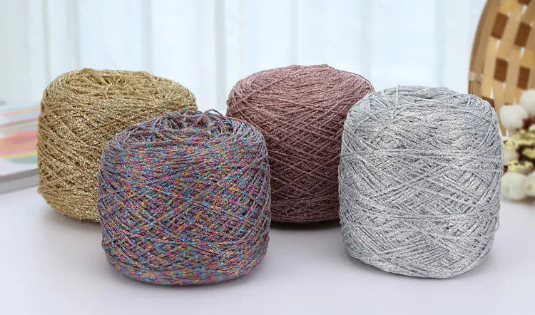 A collection of skeins of metallic silk crocheting and knitting yarn in various shades of beige, pink, and silver.
