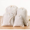 A set of ten natural off-white cotton drawstring gift bags lying on a wooden surface.