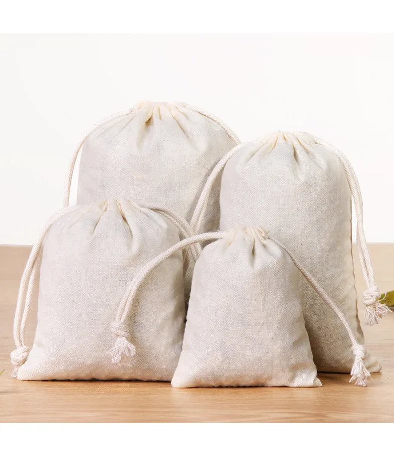 A set of ten natural off-white cotton drawstring gift bags lying on a wooden surface.