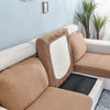 A beige stretch sofa seat cushion protector slipcover on a white sofa with light blue walls and green plants.