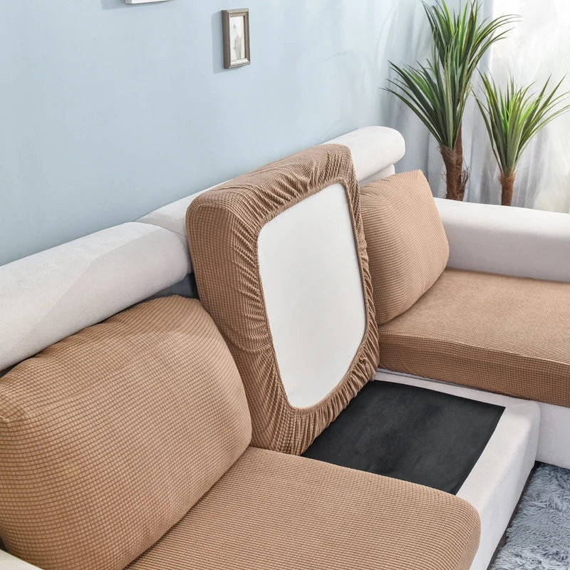 A beige stretch sofa seat cushion protector slipcover on a white sofa with light blue walls and green plants.