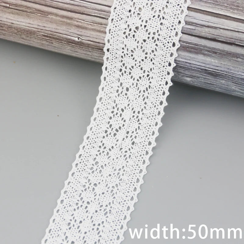 A close-up of white cotton embroidered lace trim with a scalloped edge, shown against a gray wooden surface.