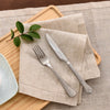 A set of linen table linens and napkins placed on a wooden board with silverware and a green leaf.