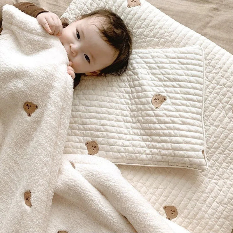 A baby is lying on a white soft coral fleece flannel blanket with quilted texture and small brown appliqués.