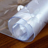 Roll of transparent PVC tablecloth material with a floral pattern resting on a wooden surface.
