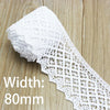 A roll of white cotton embroidered lace trim with a width of 80mm lying on a wooden surface.