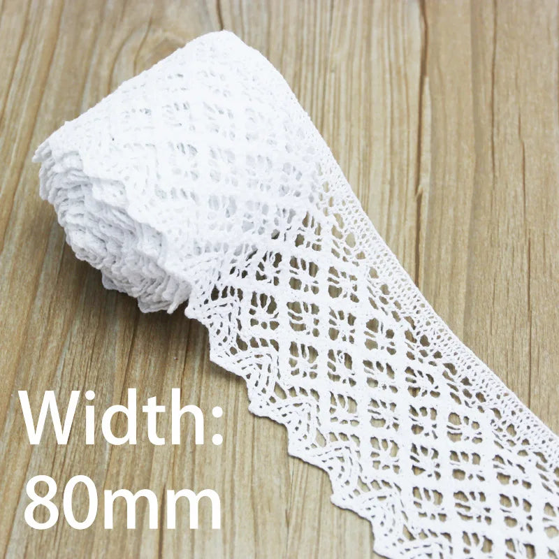 A roll of white cotton embroidered lace trim with a width of 80mm lying on a wooden surface.