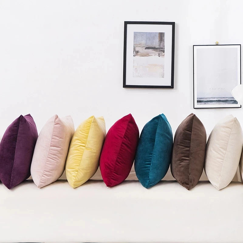 A row of solid velvet decorative cushion covers in various shades including purple, pink, yellow, red, teal, brown, and cream
