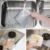 A hand is pouring water onto a reusable non-stick gas stove cleaning mat inside a stainless steel sink.