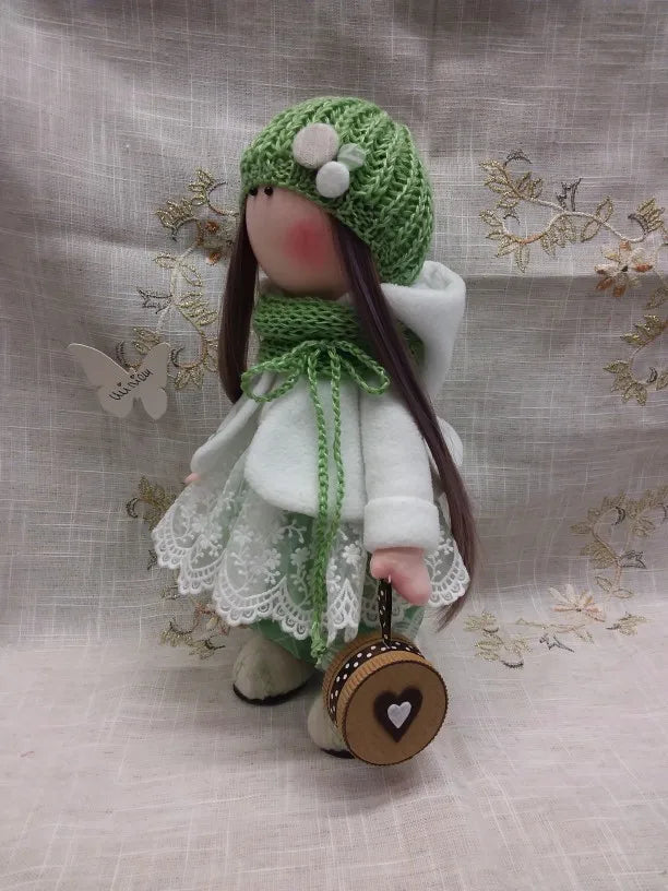A handmade cotton toy filler batting doll with a green knitted hat and white clothing.