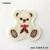 A cream-colored embroidered bear patch with brown accents and a red bow.