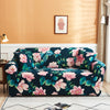 A dark floral patterned stretch fabric sofa cover displayed on a light rug against an orange wall.