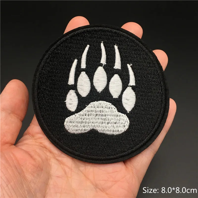 A hand holds a black embroidered punk badge featuring a white paw print design.