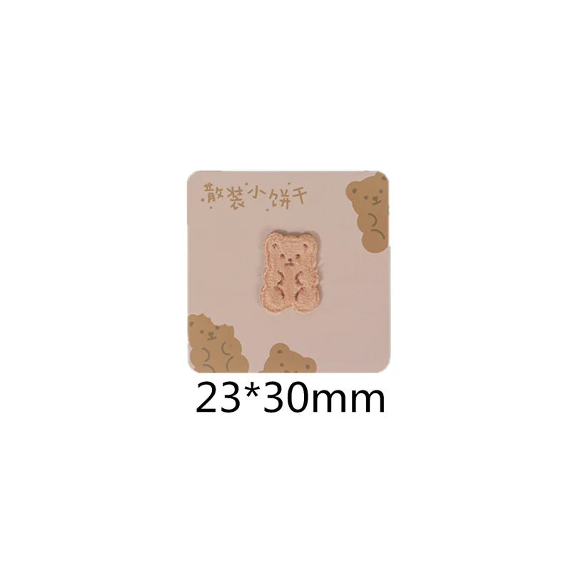 A square beige iron-on patch featuring a light brown, fluffy bear embroidery.
