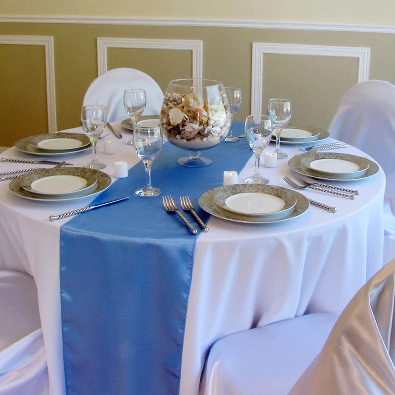 A round table set for an event featuring a blue satin table runner, white linens, and glassware.