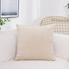 A beige velvet decorative cushion cover resting on a white sofa next to a gold wire chair and framed artwork.