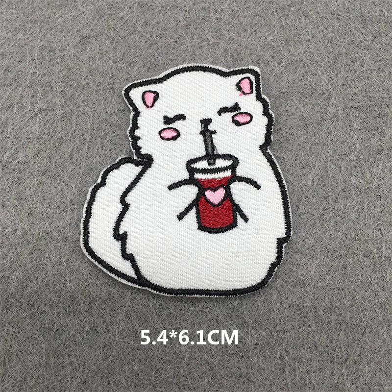A white cat embroidered patch with pink accents, holding a red cup.